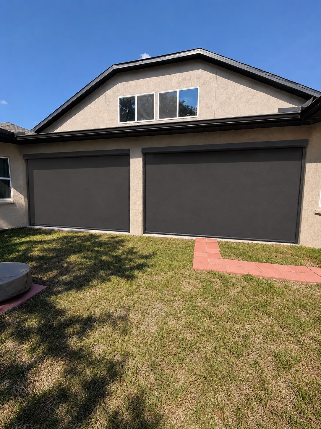 Two motorized exterior screens fully lowered, enclosing a covered lanai on a stucco home